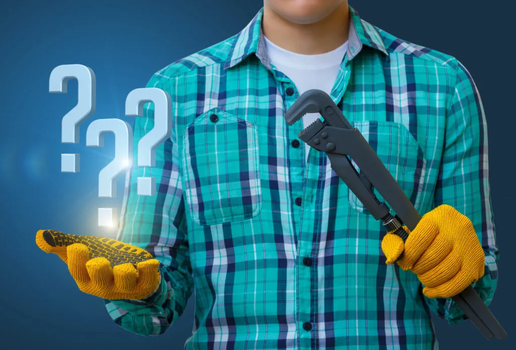 Plumber answers questions. Worker on a blue background with a spanner and questions in hand.