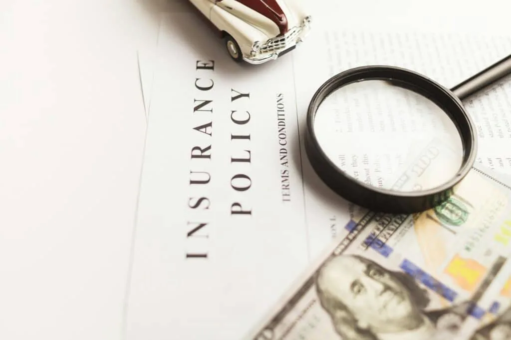 an image of toy car, magnifying glass and a bill on top of insurance claim policy.